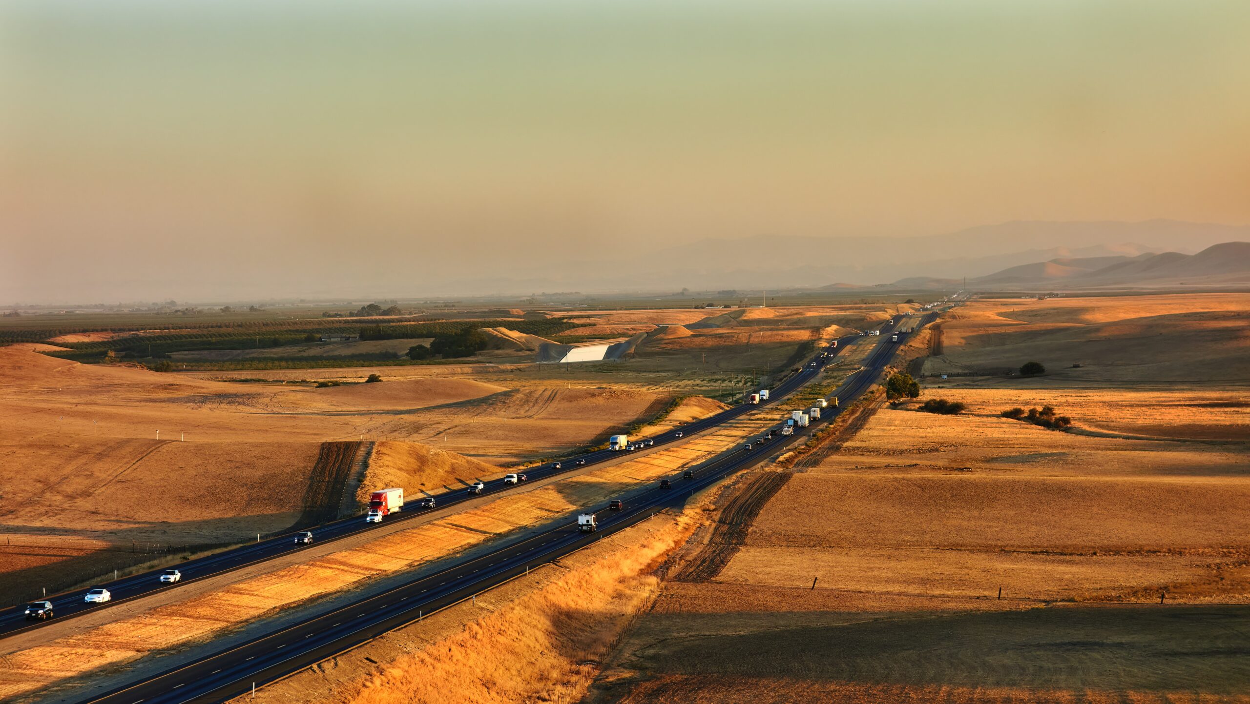 Image of trucks on a highway driving through a yellow field.
